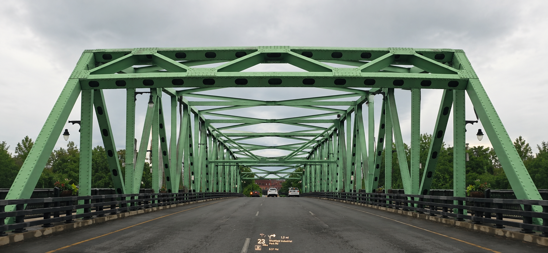 Green truss bridge spanning a calm roadway