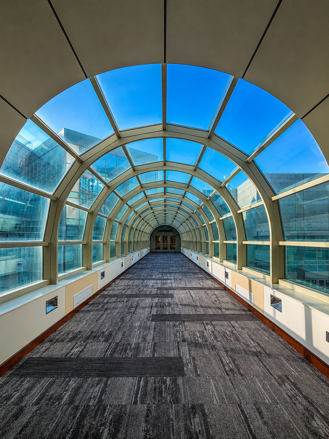 Glass and steel hospital walkway beneath a bright blue sky